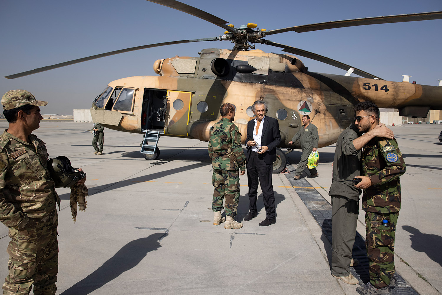 Bernard-Henri Lévy et quatre militaires sur la piste d'un aéroport à Kaboul devant un hélicoptère militaire