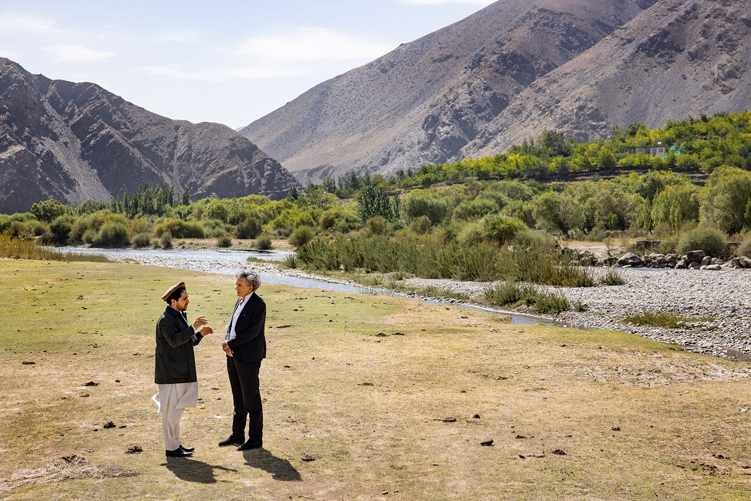 Bernard-Henri Lévy et Ahmad Massoud près d'une rivière bordée d'arbres avec à l'arrière plan les montagnes du Panjshir.