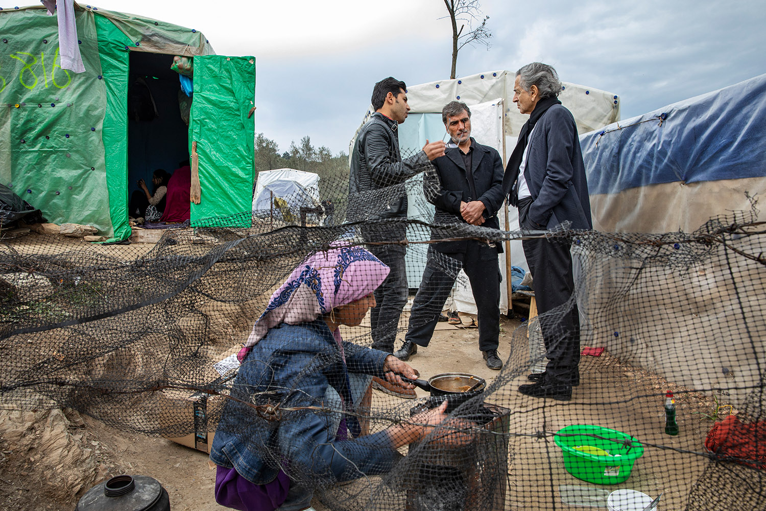 Bernard-Henri Lévy parle avec deux hommes au milieu des tentes du camp de Moria à Lesbos.