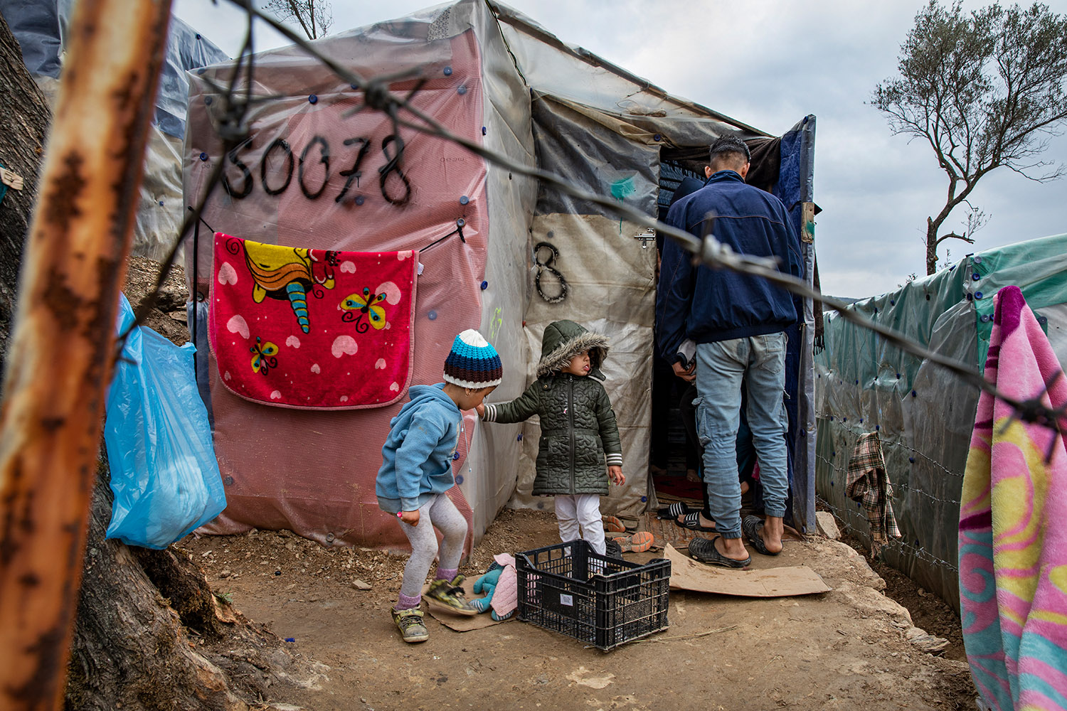 Des enfants devant une tente du camp de migrants de Moria à lesbos, derrière des barbelés.