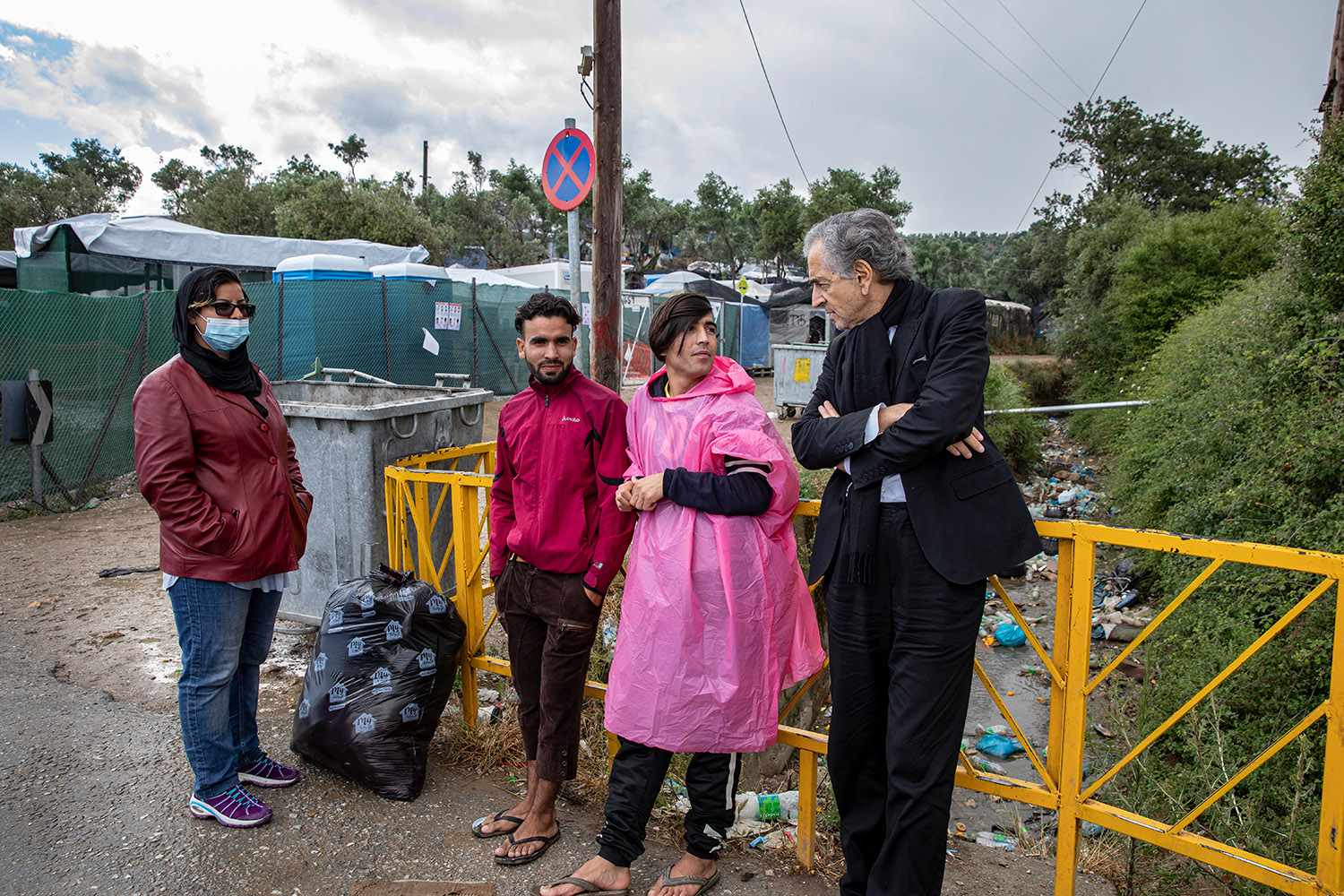 Bernard-Henri Lévy parle avec trois migrants à Moria au milieu des tentes, de la boue et des déchets.