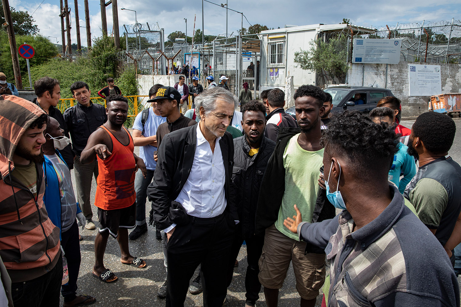 Bernard-Henri Lévy écoute un groupe de réfugiés à l'entrée du camp de Moria à Lesbos.