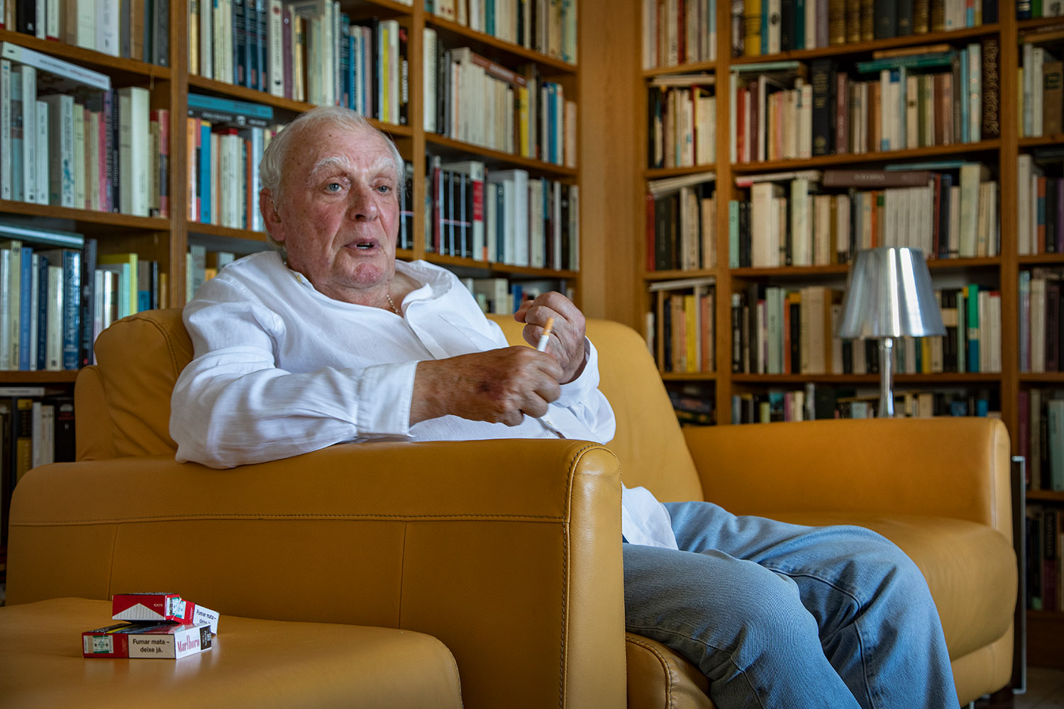 Antonio Lobo Antunes assis dans un canapé dans sa bibliothèque.