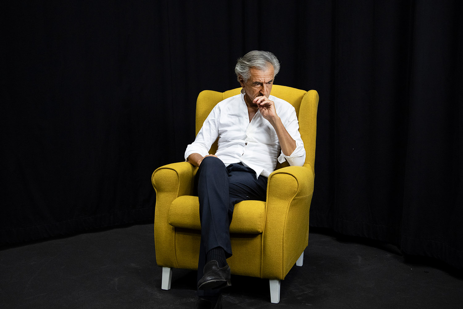 Bernard-Henri Lévy assis dans un fauteuil jaune.