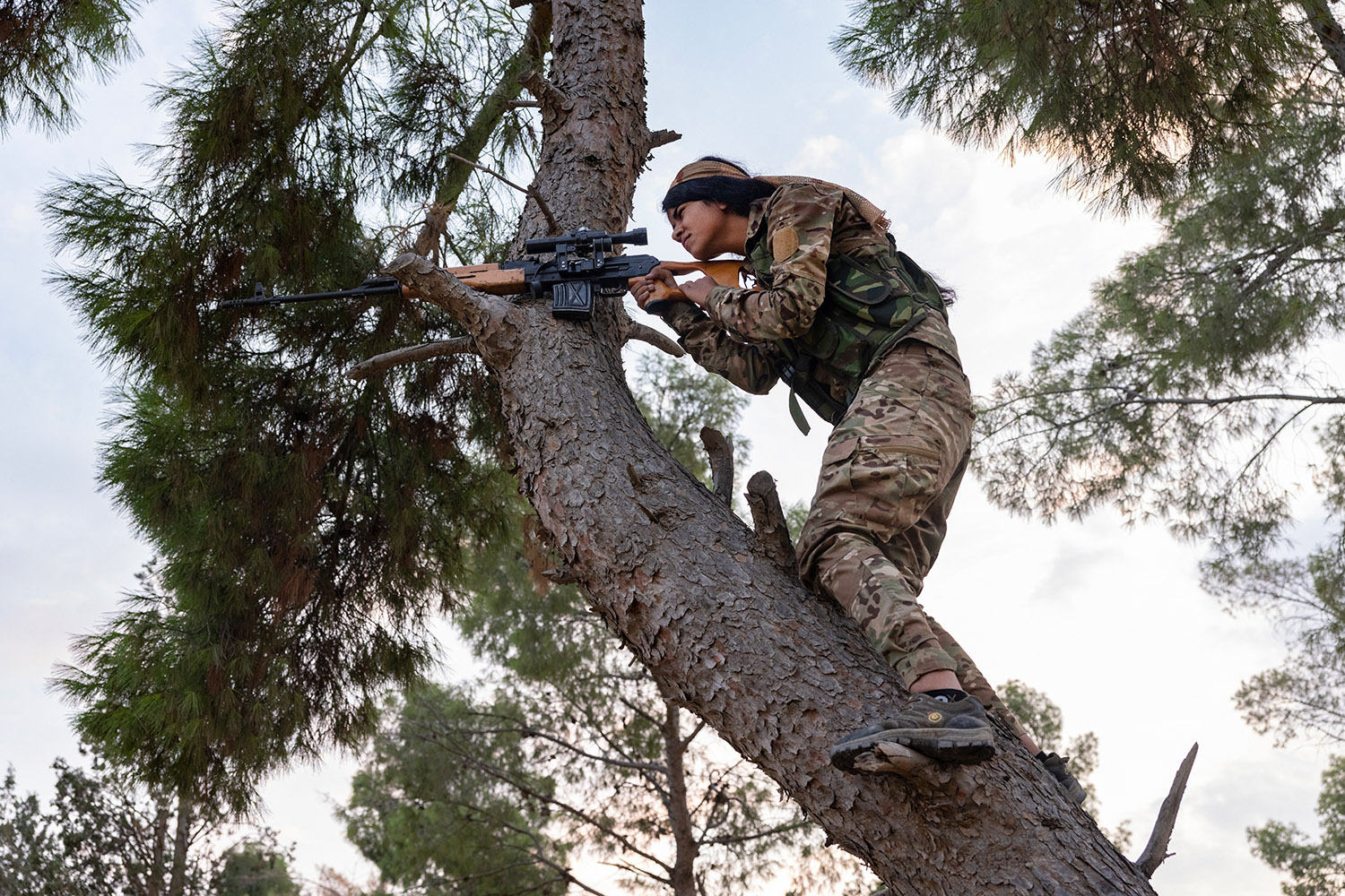 Femme soldat kurde dans un arme, elle vise à travers son arme posée sur une branche.