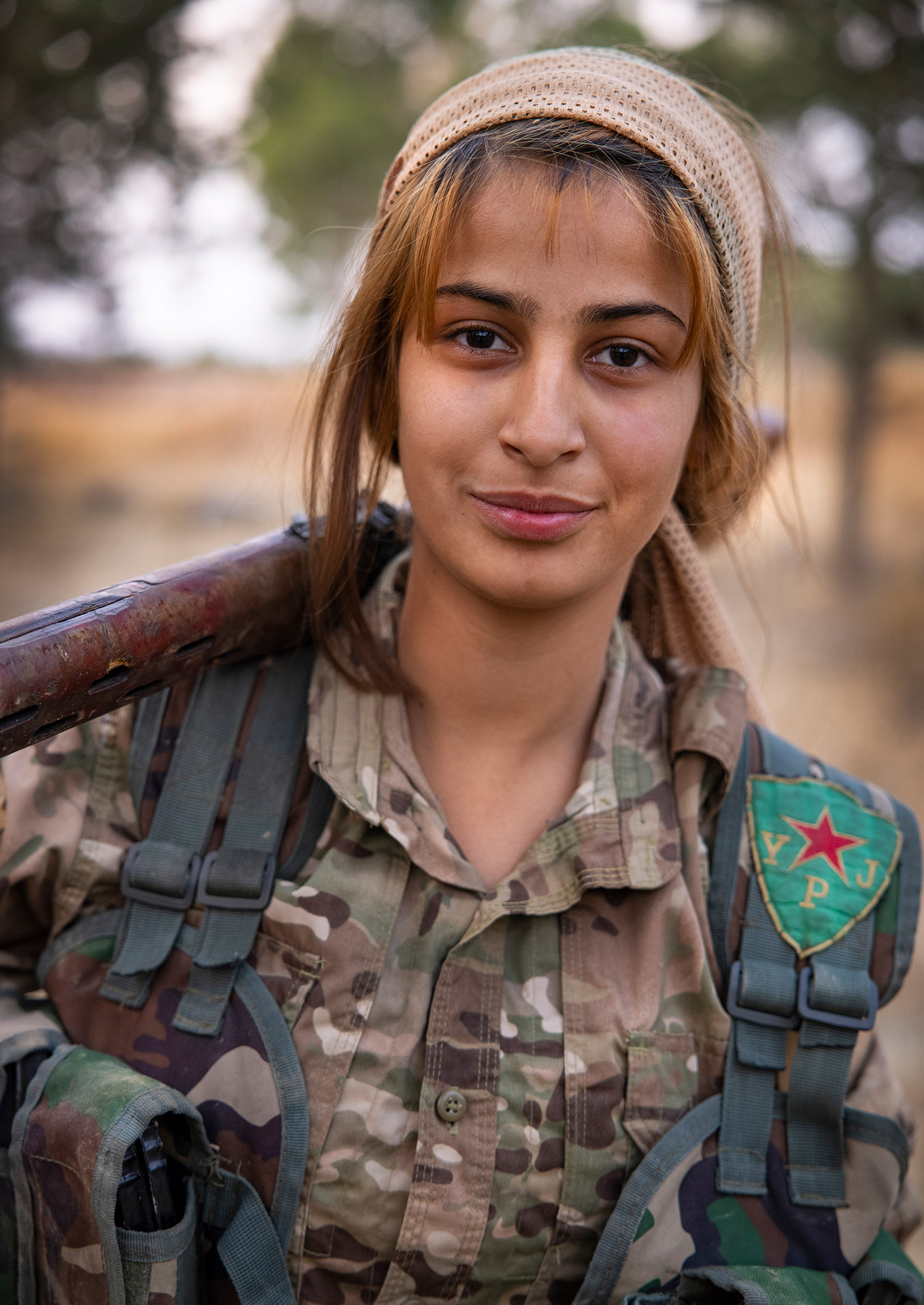 Portrait d'une femme soldat, elle est en uniforme, et porte sur arme sur son épaule.