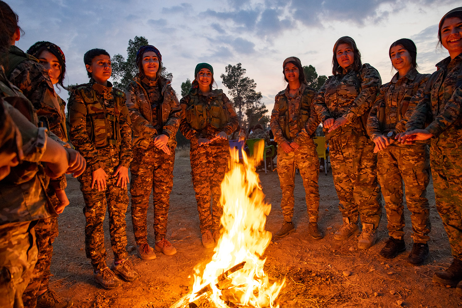 Les femmes-soldats en tenue militaire debouts en rond autour d'un feu à la tombée du jour.