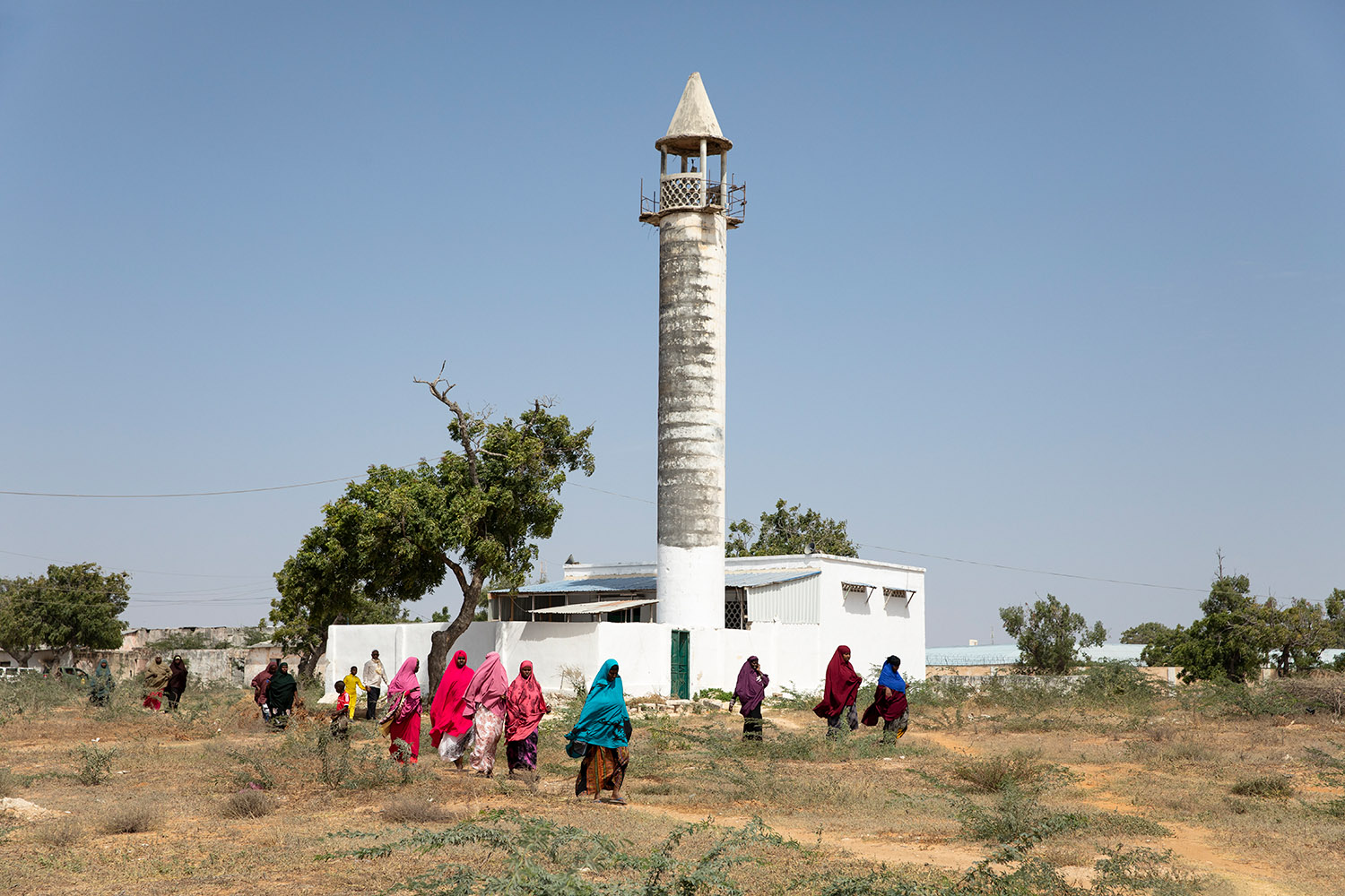 Des femmes portent des abayas multicolores sur une terrain vague près d'un minaret.