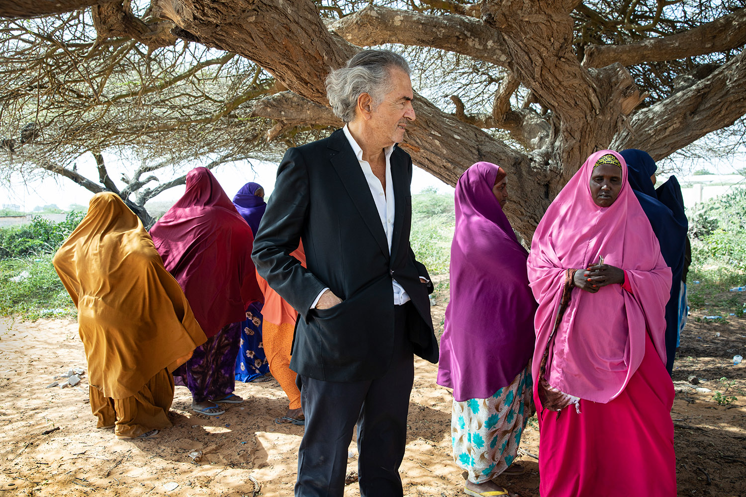 Bernard-Henri Lévy et les femmes de Mogadiscio, qui portent des abayas multicolores, sous un arbre.