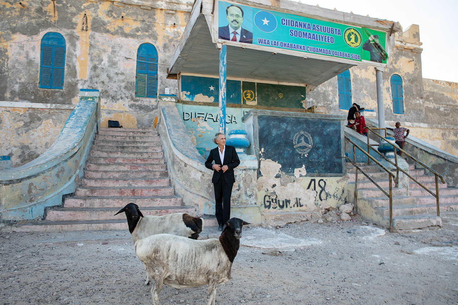 Bernard-Henri Lévy dans une rue de Mogadiscio, il y a des chèvres et premier plan.