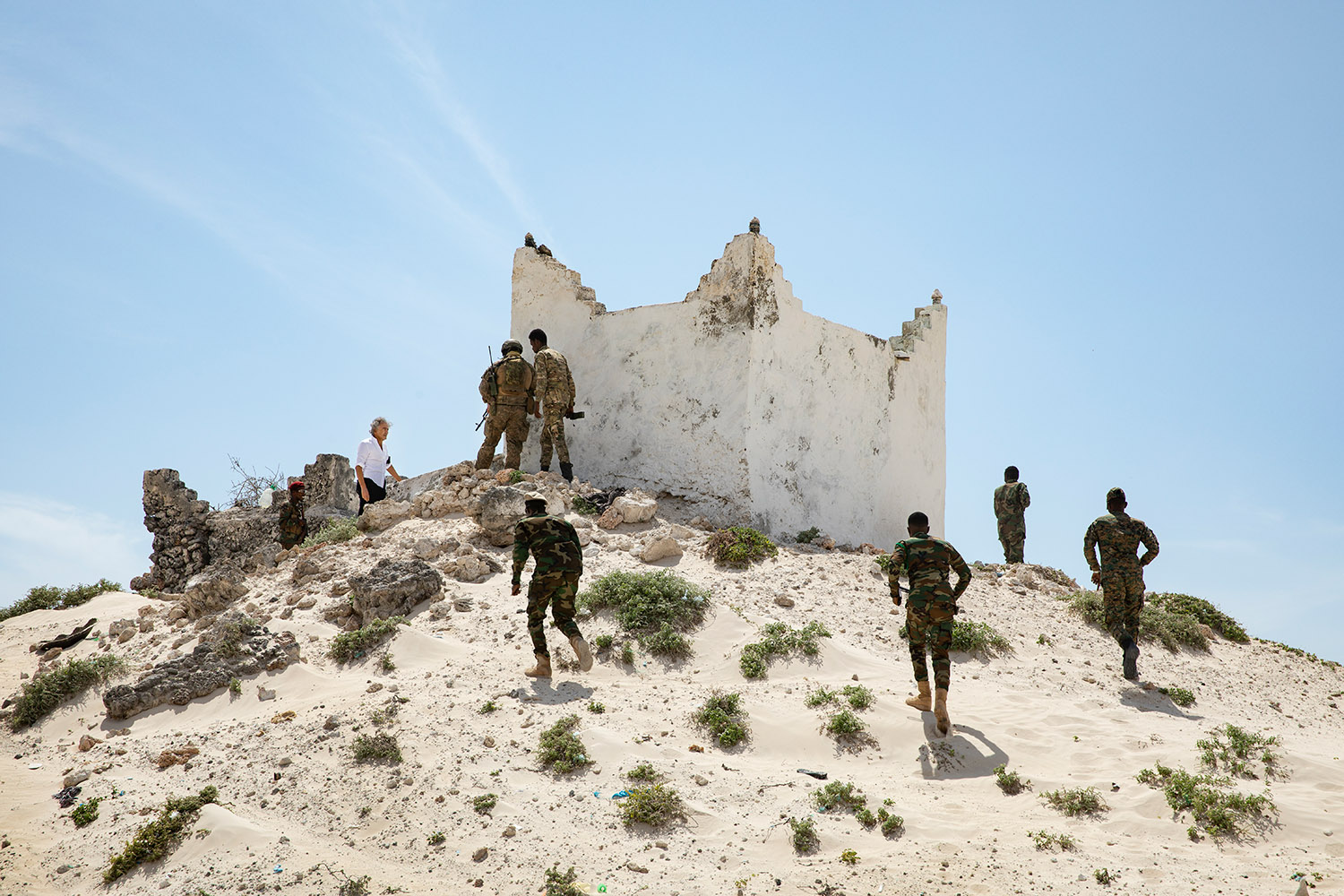 Des militaires montent en haut d'une colline de sable au sommet duquel se trouve une petite maison de pierre