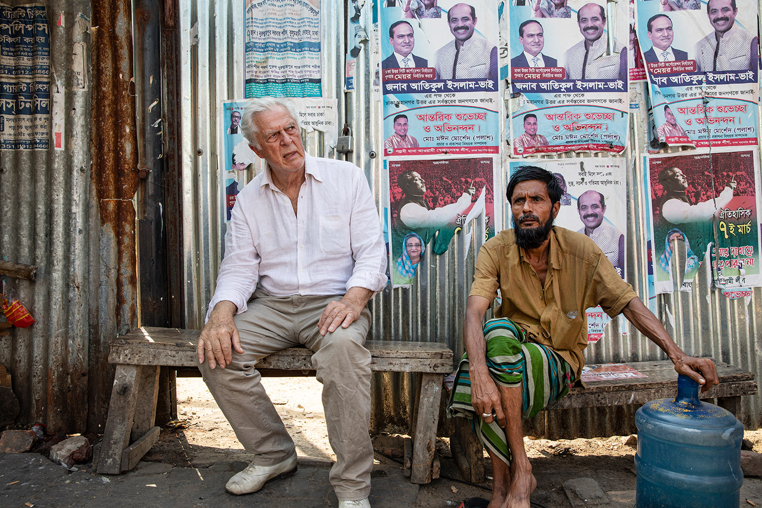 Dans une rue de Dacca, Gilles Hertzog est assis sur un banc à côté d'un habitant de Dacca.
