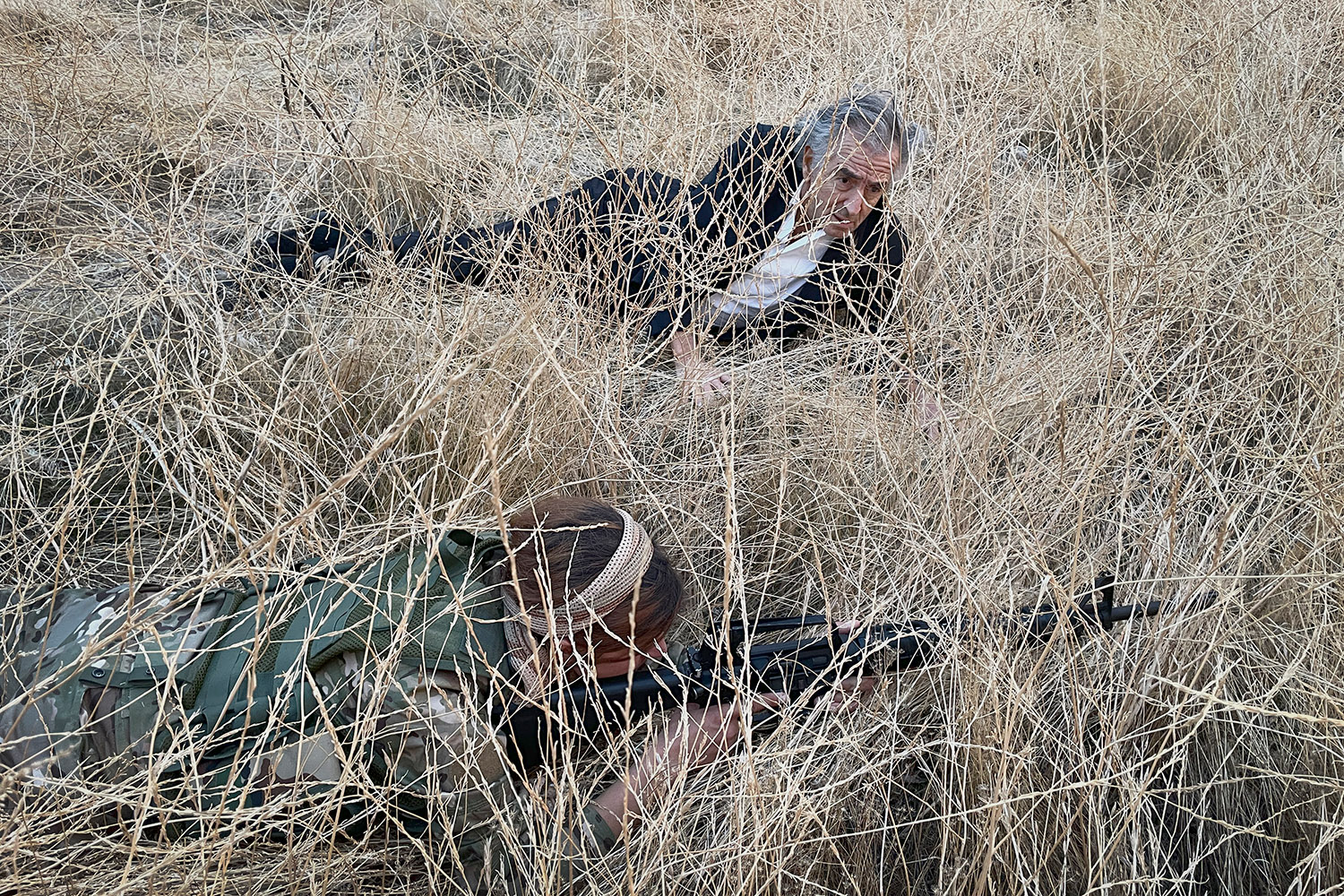 Au Rojava, à Maaluja en novembre 2020, Bernard-Henri Lévy, couché dans l'herbe auprès d'une combattante kurde, assiste à un entraînement militaire.