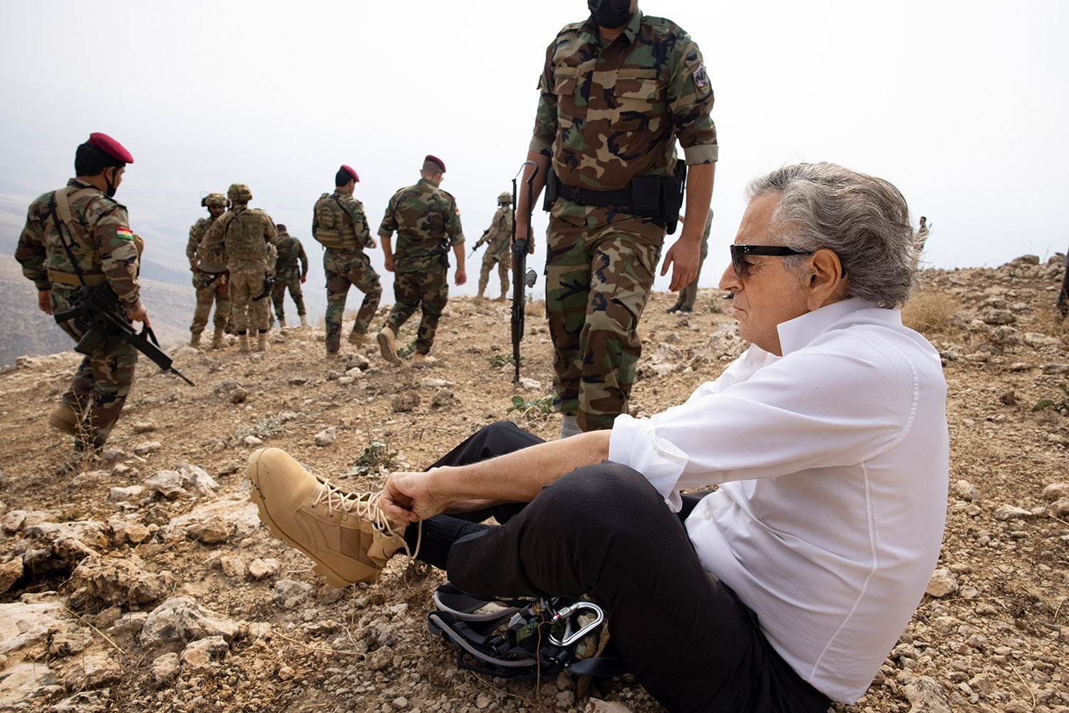 Sur la crête de Karachok au Kurdistan irakien, Bernard-Henri Lévy se prépare à descendre dans une grotte de Daech et revêt ainsi son équipement entouré par les peshmergas.