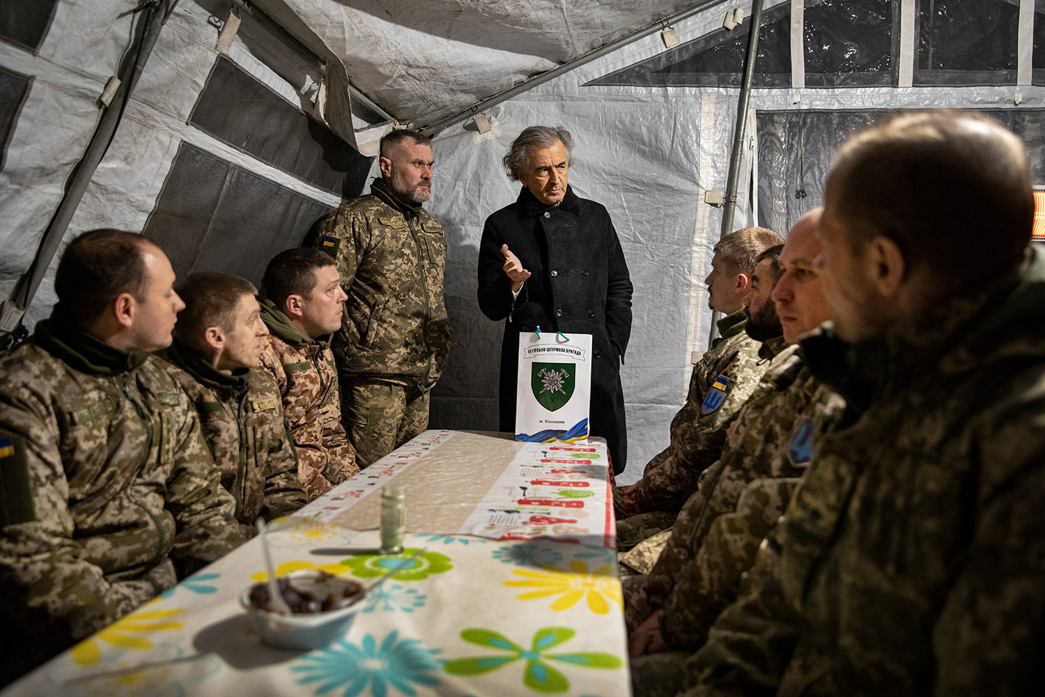 Bernard-Henri Lévy parle à des militaires assis autour d'une table sous une tente.