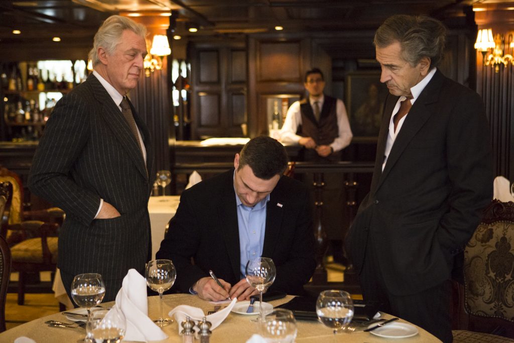 Rencontre entre Vitali Klitschko (au centre), Bernard-Henri Levy (à droite) et Gilles Hertzog (à gauche), à Kiev le 3 mars 2014, dans un restaurant. Klitschko signe ou écrit sur un document, sous le regard de Lévy et Hertzog.