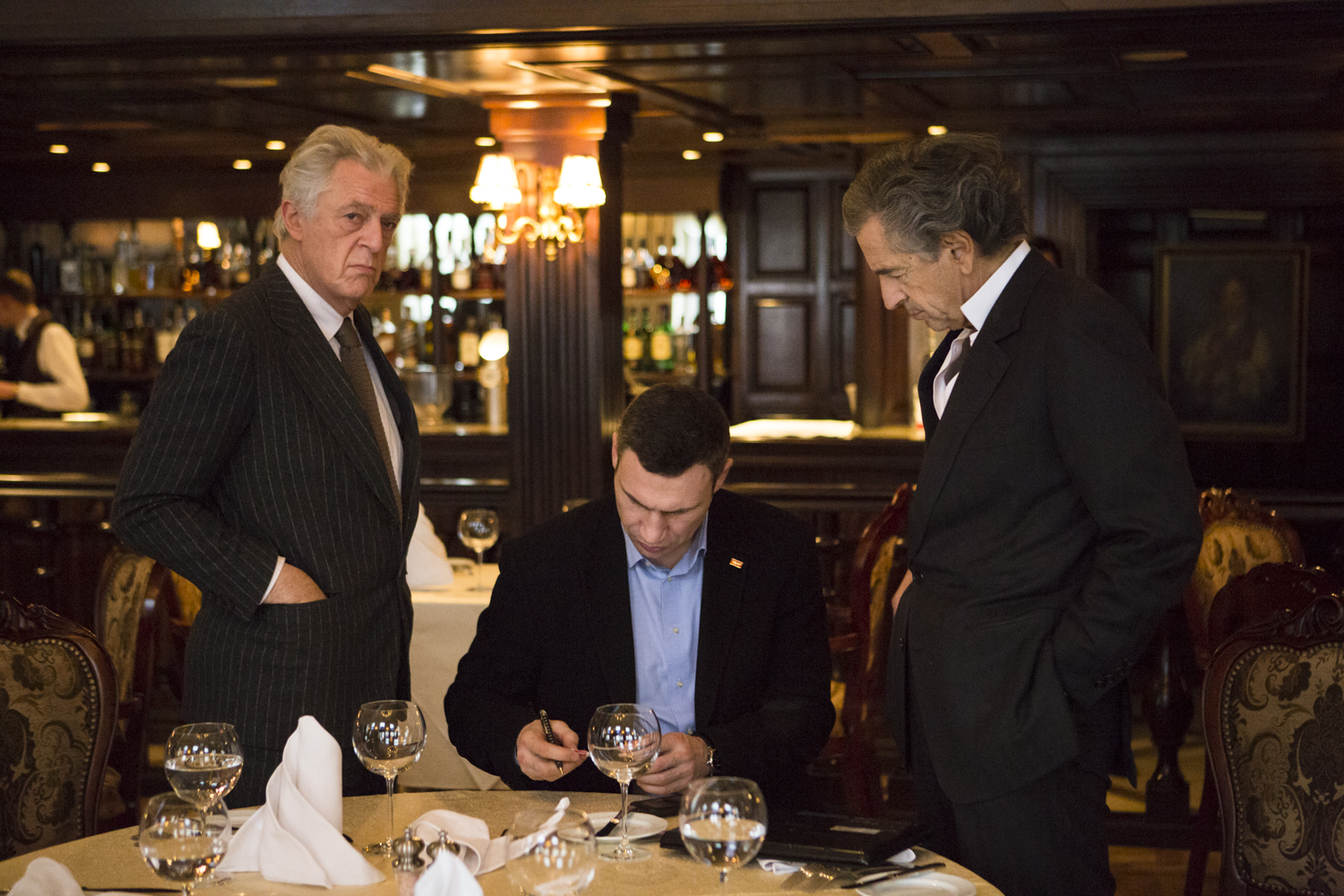 Rencontre entre Vitali Klitschko (au centre), Bernard-Henri Levy (à droite) et Gilles Hertzog (à gauche), à Kiev le 3 mars 2014, dans un restaurant. Klitschko signe ou écrit sur un document, sous le regard de Lévy et Hertzog.