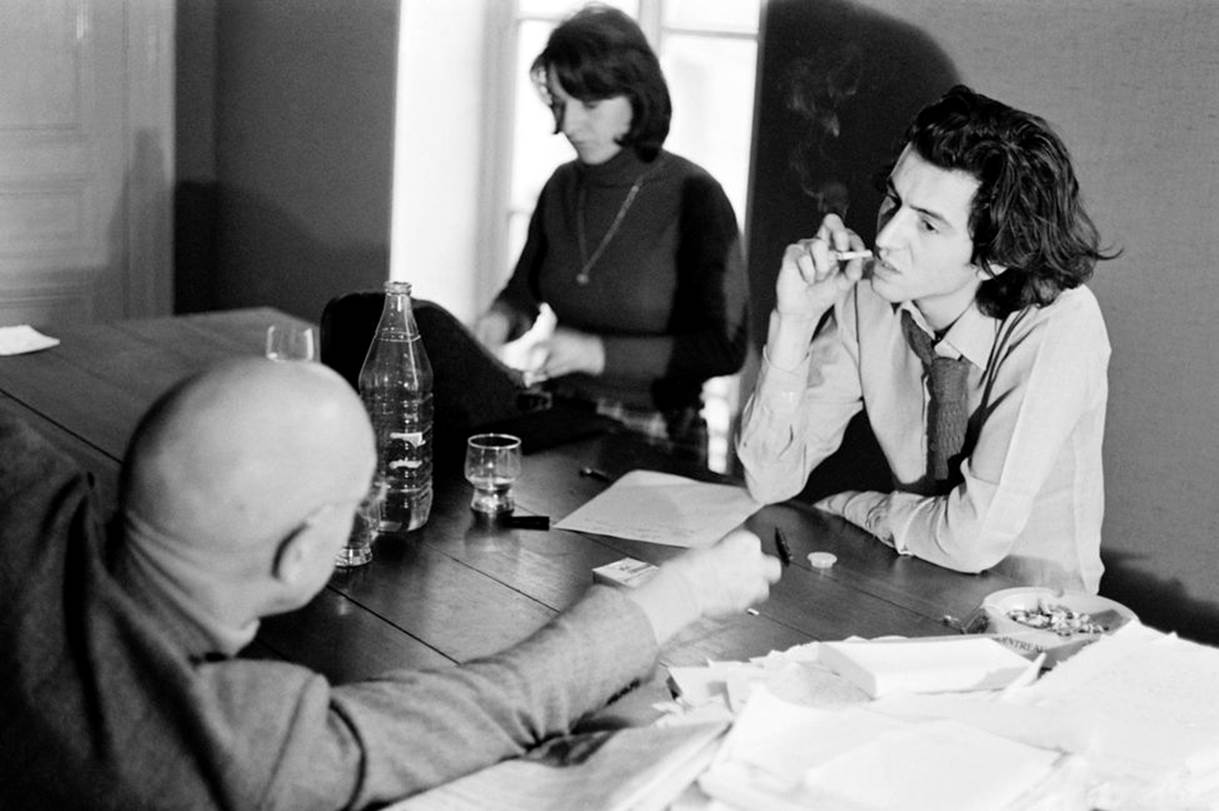 Michel Foucault et BHL dialoguent autour d'une table. Michel Foucault est de dos, Benard-Henri Lévy qui fume une cigarette est de face.