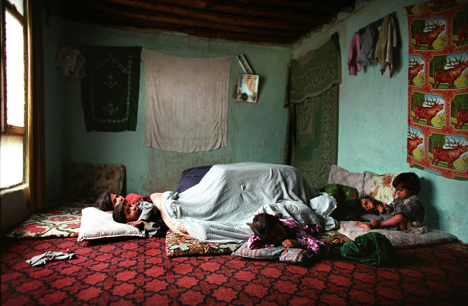 Dans la maison d'une famille afghane, les enfants dorment ensemble par terre sur des coussins et des tapis/