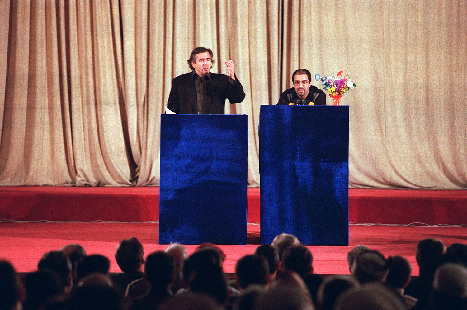 Bernard-Henri Lévy et Atiq Rahimi, prennent la parole sur une scène devant une assemblée.