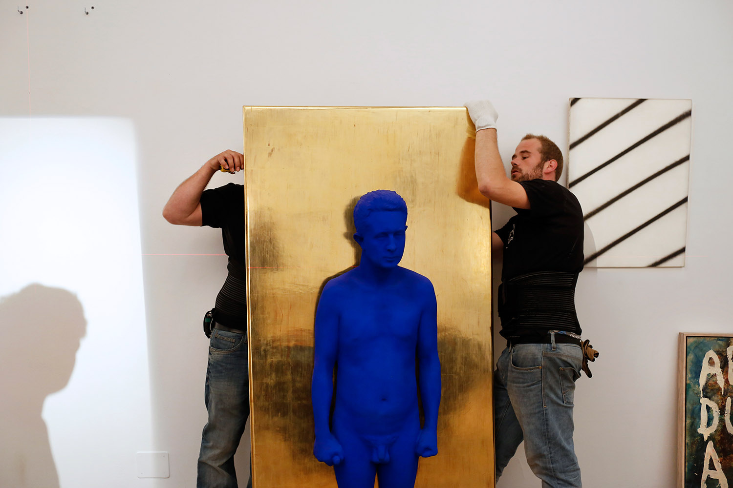 Accrochage d'une sculpture bleue d'Yves Klein. Elle représente un homme sur un fond doré