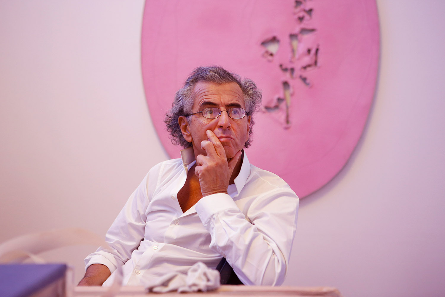 Bernard-Henri Lévy est assis devant des oeuvres dans une salle de la Fondation Maeght
