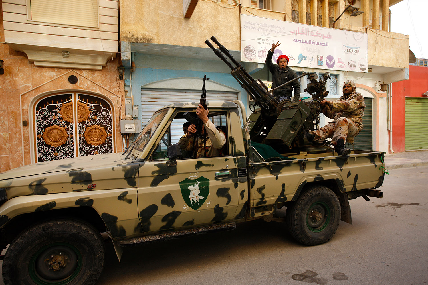 Dans une jeep militaire, qui porte de l'artillerie à l'arrière du véhicule, des hommes font le signe V de la victoire et portent haut leurs mitraillettes.