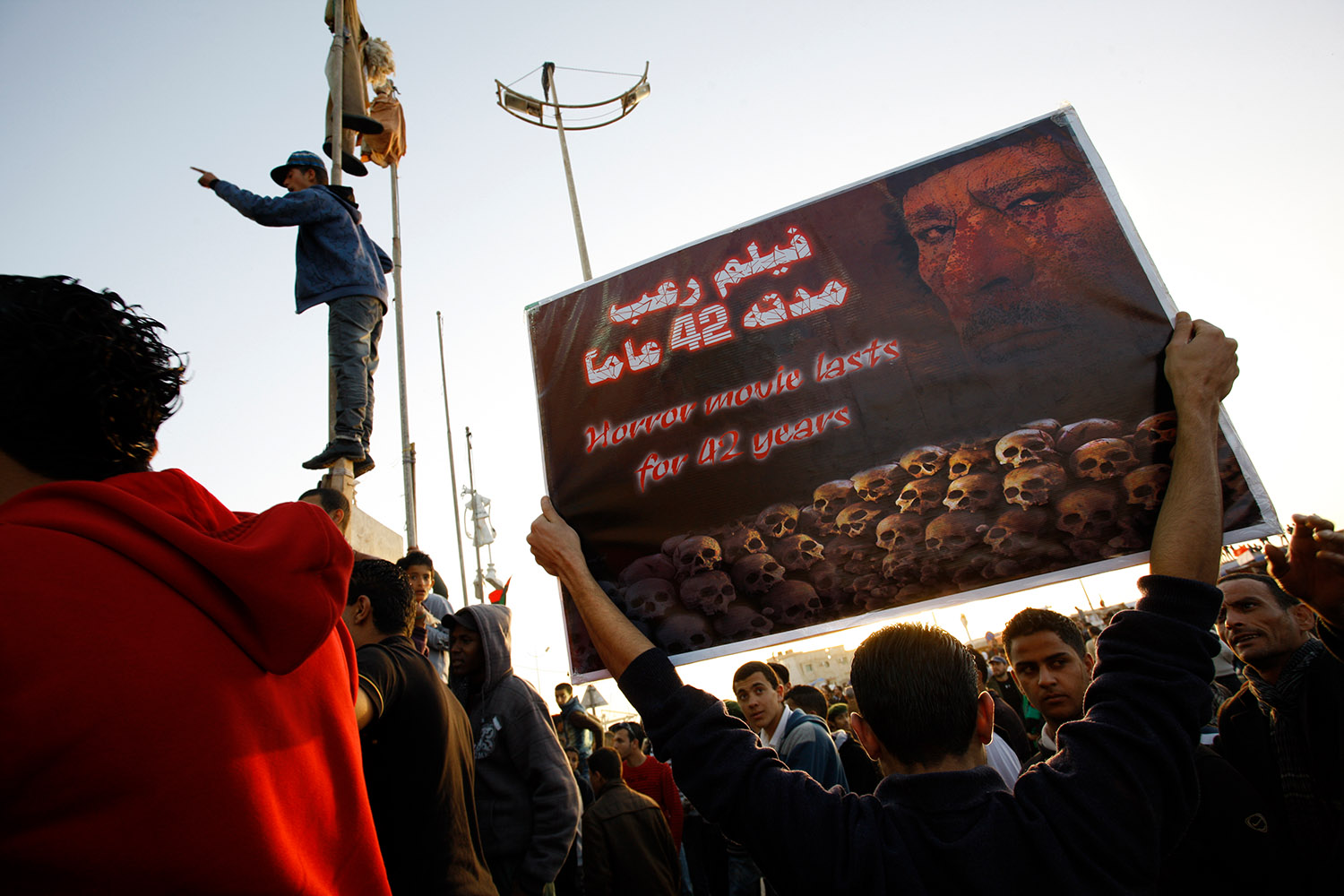 A Benghazi, un manifestant présente le régime de Kadhafi comme un « film d'horreur qui dure depuis 42 ans ». Parmi la foule sa pancarte représente des têtes de mort et le visage de Kadhafi.