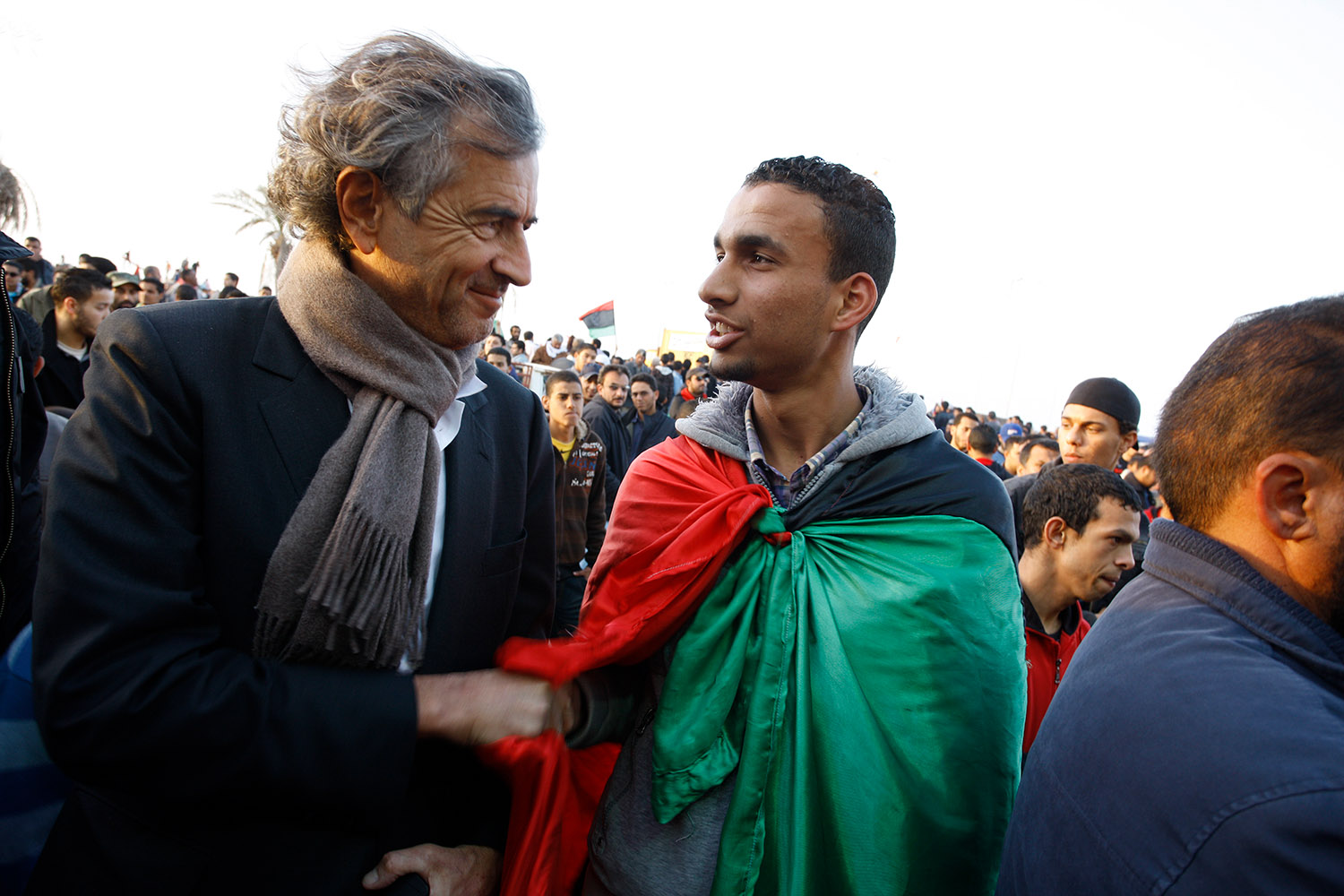 Bernard-Henri Lévy à Benghazi, parmi la foule de la Révolution des jeunes. Il parle et sert la main d'un jeune manifestant qui porte sur ses épaules le drapeau de la Libye.