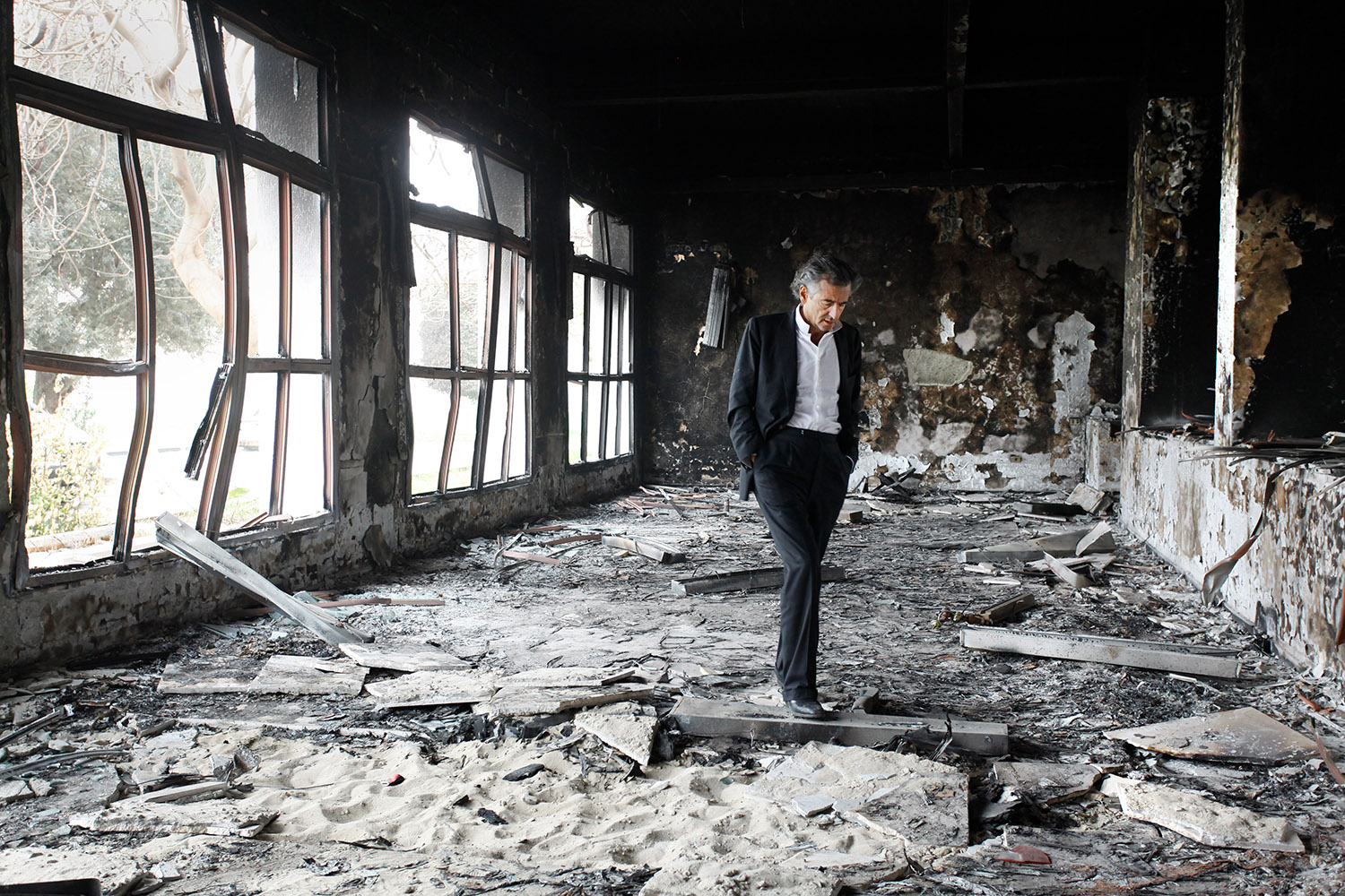Bernard-Henri Lévy, dans les ruines de Benghazi. Seuil, il marche au milieu des débris et des cendres.