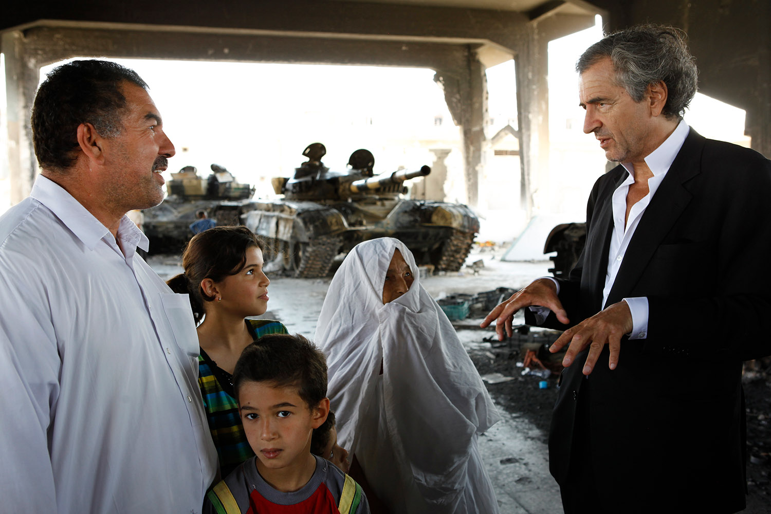 Bernard-Henri Lévy à la rencontre des Libyens à Misrata. BHL parle avec un homme, une femme et deux enfants. Derrière eux il y a des chars.