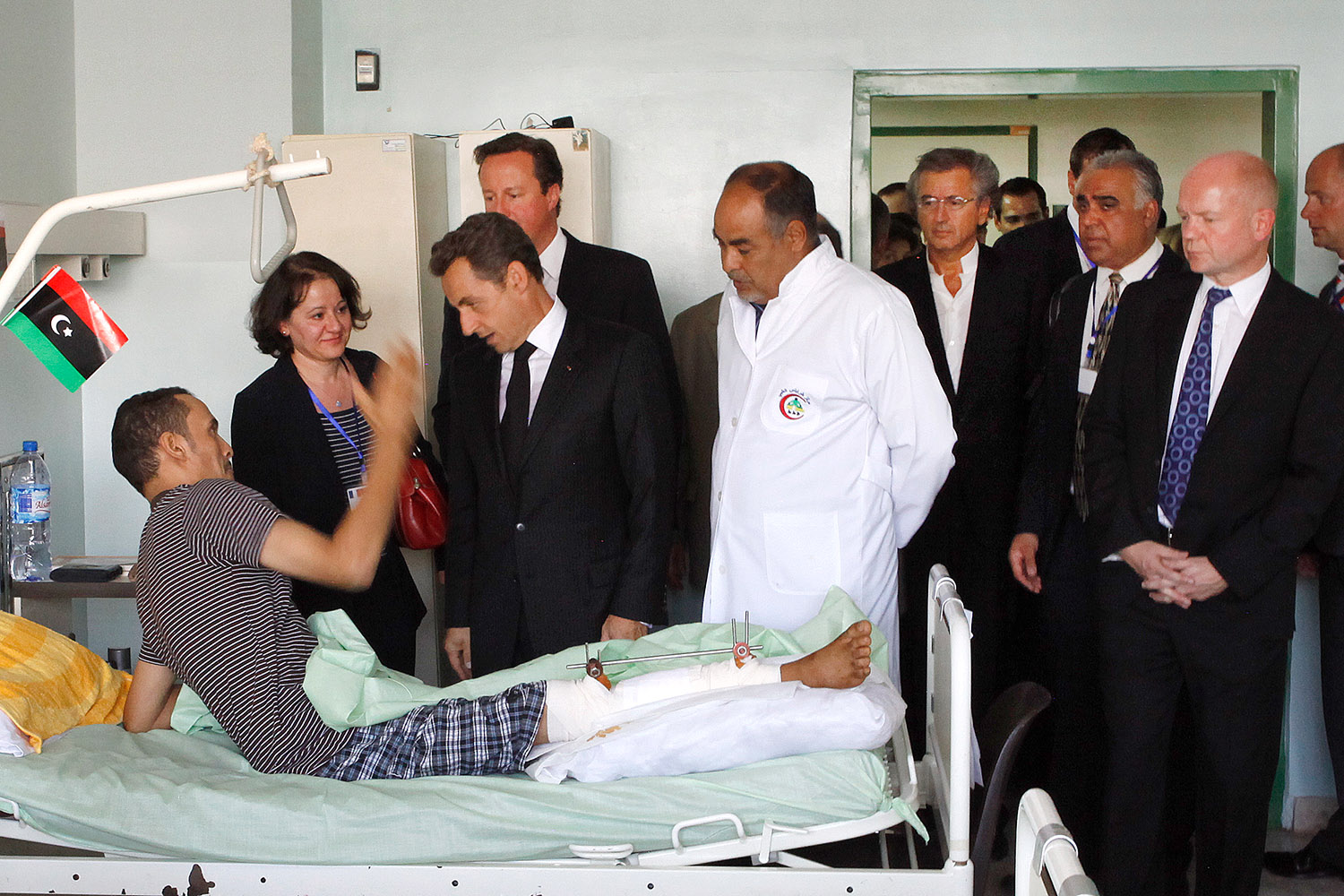 Bernard-Henri Lévy accompagne Nicolas Sarkozy et James Cameron à l'hôpital de Tripoli, rendre visite aux victimes de la barbarie kadhafiste. Il y a également un médecin et le personnel des hommes politiques. Un hommes est allongé sur son lit d'hopital, un a un plâtre et du métal dans la jambe.