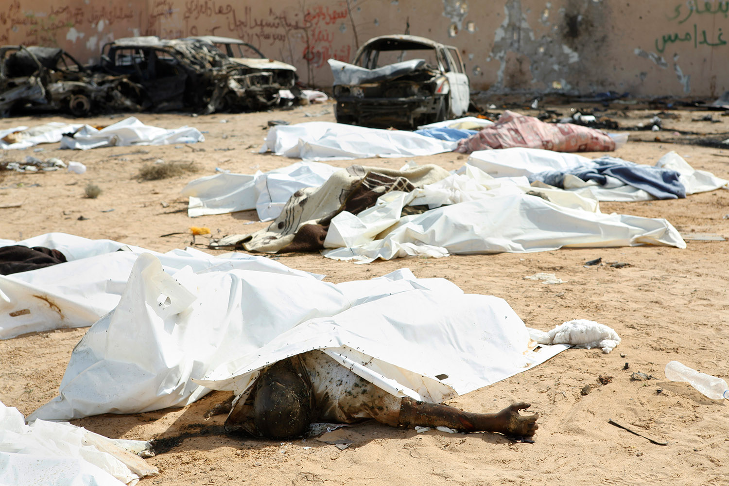 Sur le sable de Syrte en Libye, des cadavres couverts de plastiques blancs, et de mouches, au milieu de carcasses de voitures carbonisées.