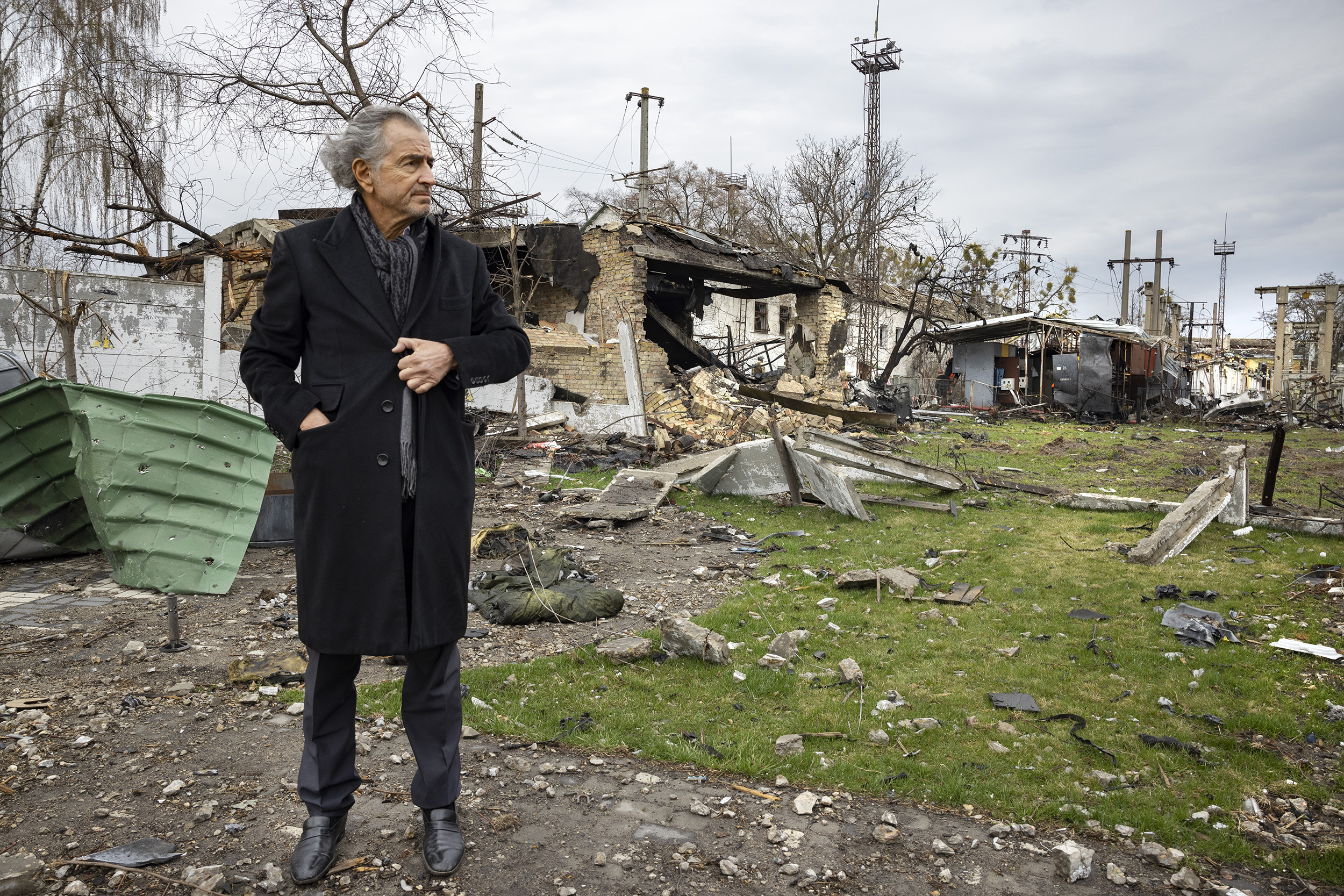 Bernard-Henri Lévy dans les ruines de la ville d'Andreevka. Une maison a brûlée, explosée. Il y a des débris au sol.