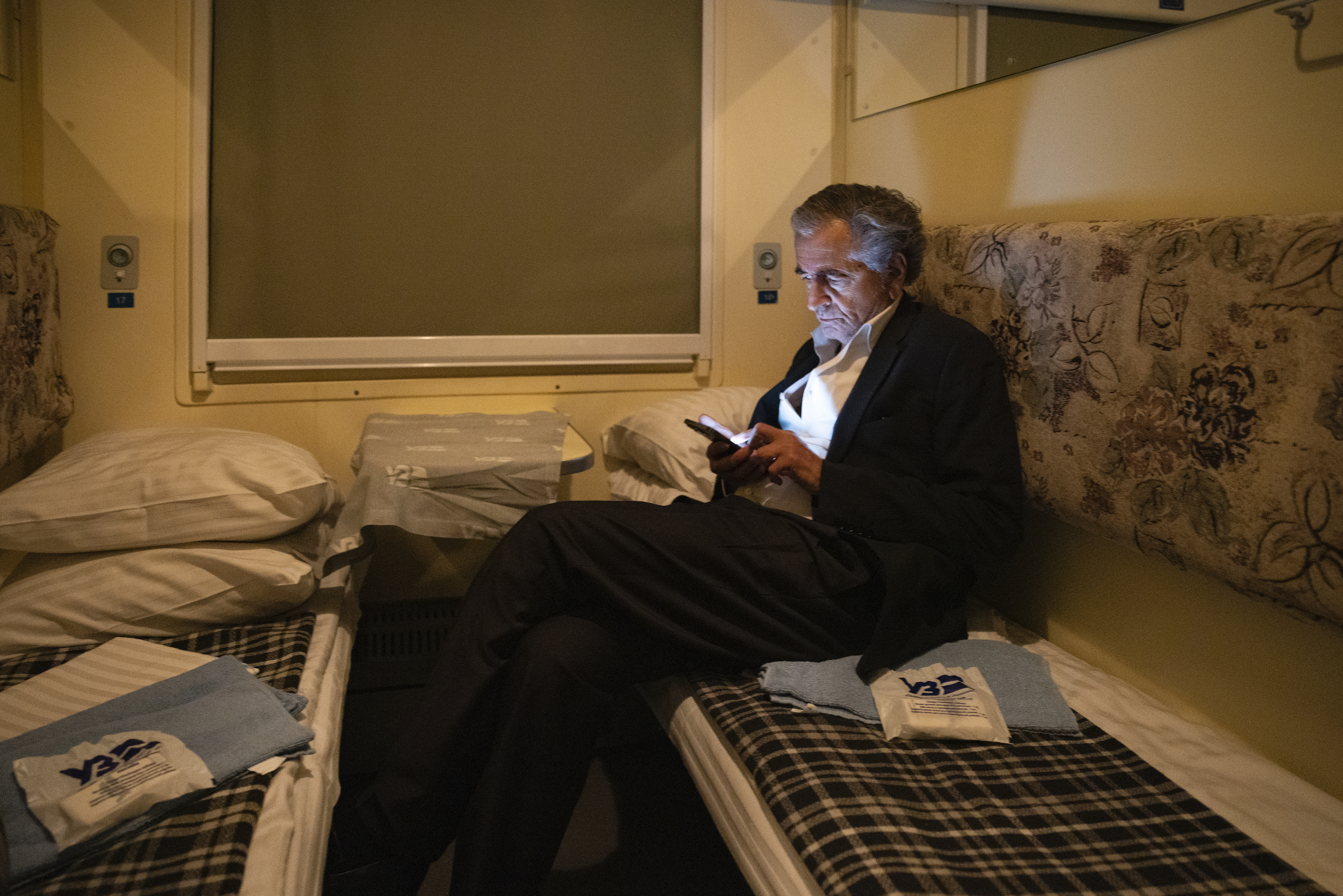 Bernard-Henri Lévy est assis sur la couchette d'un train sur laquelle il consulte son téléphone portable.