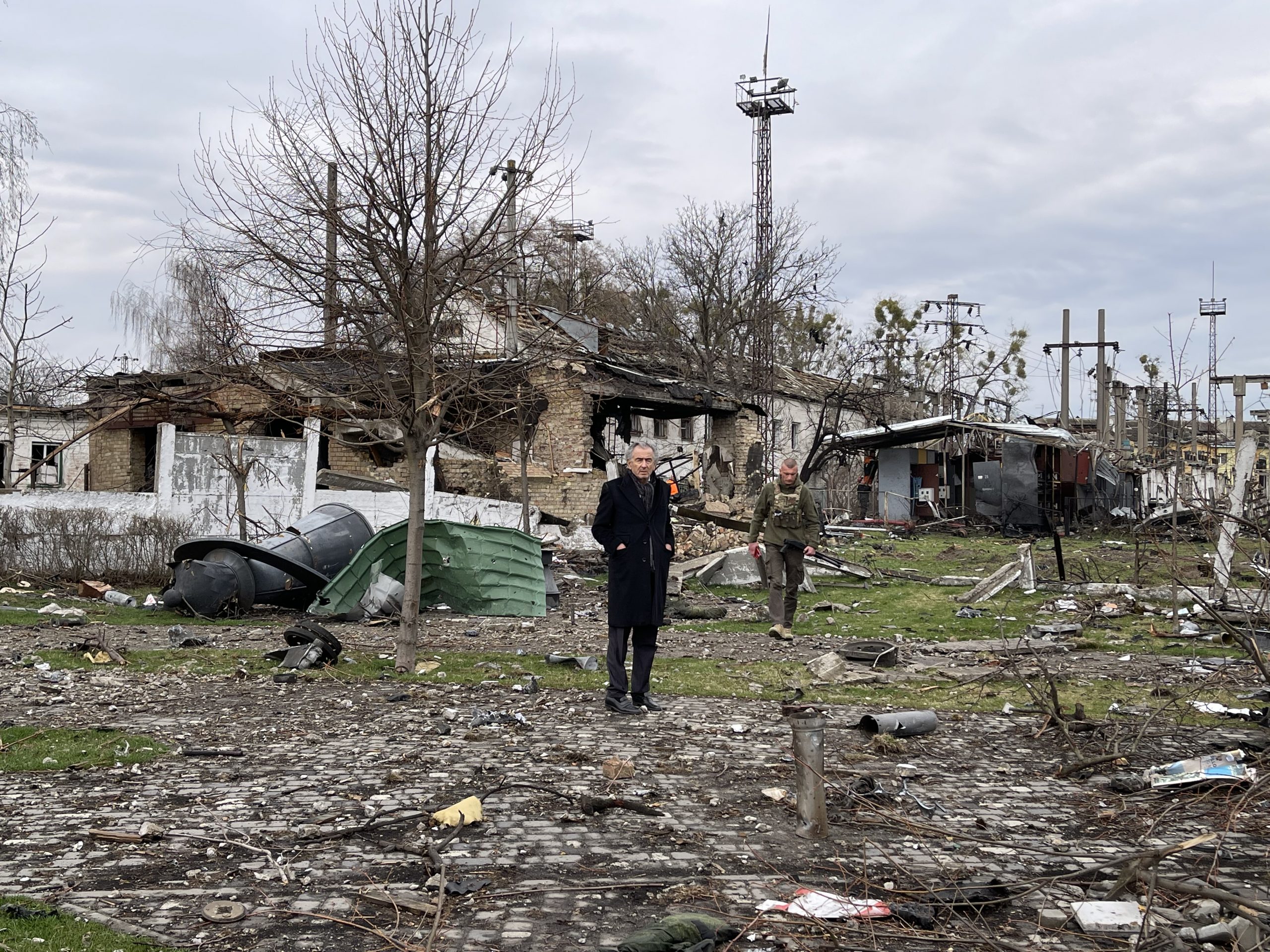 Bernard-Henri Lévy au milieu des ruines de Boradyanka en Ukraine. Des débris jonchent le sol, une maison a brûlée suite à une explosion.