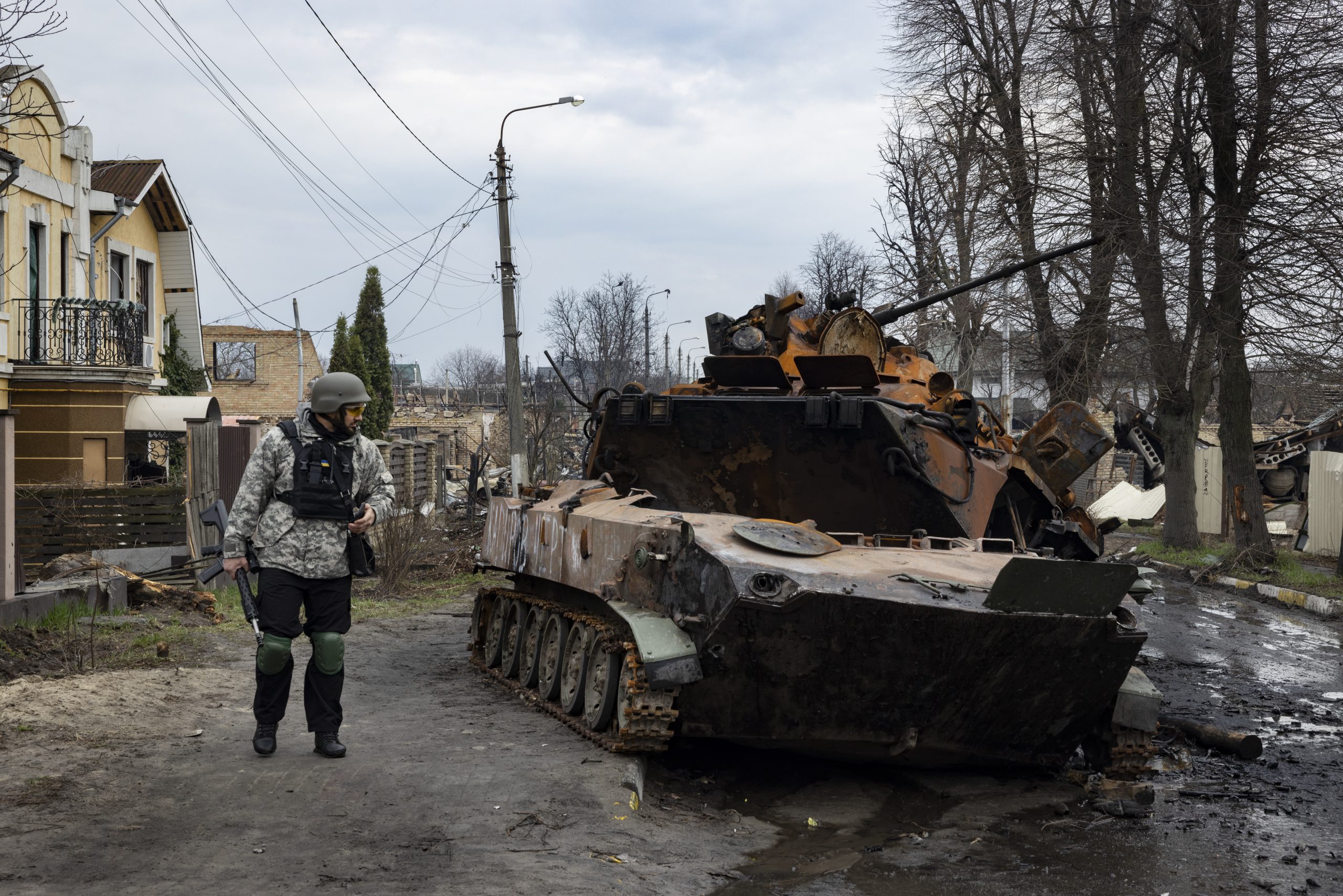 Un tank détruit dans un rue de Boutcha en Ukraine. Un militaire à gauche du tank éventré l'observe.