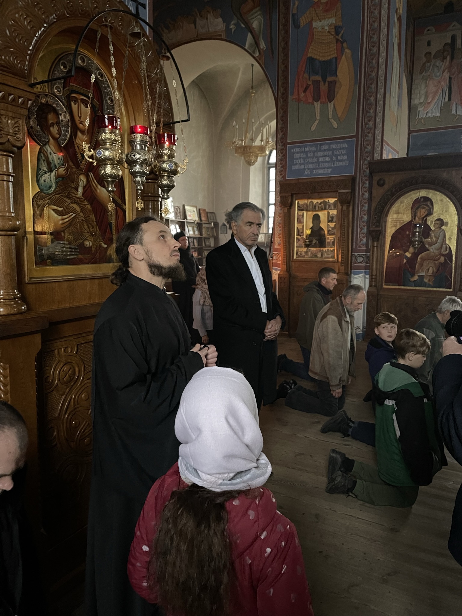 Bernard-Henri Lévy dans un monastère orthodoxe en Ukraine. Il est entouré des fidèles qui prient.