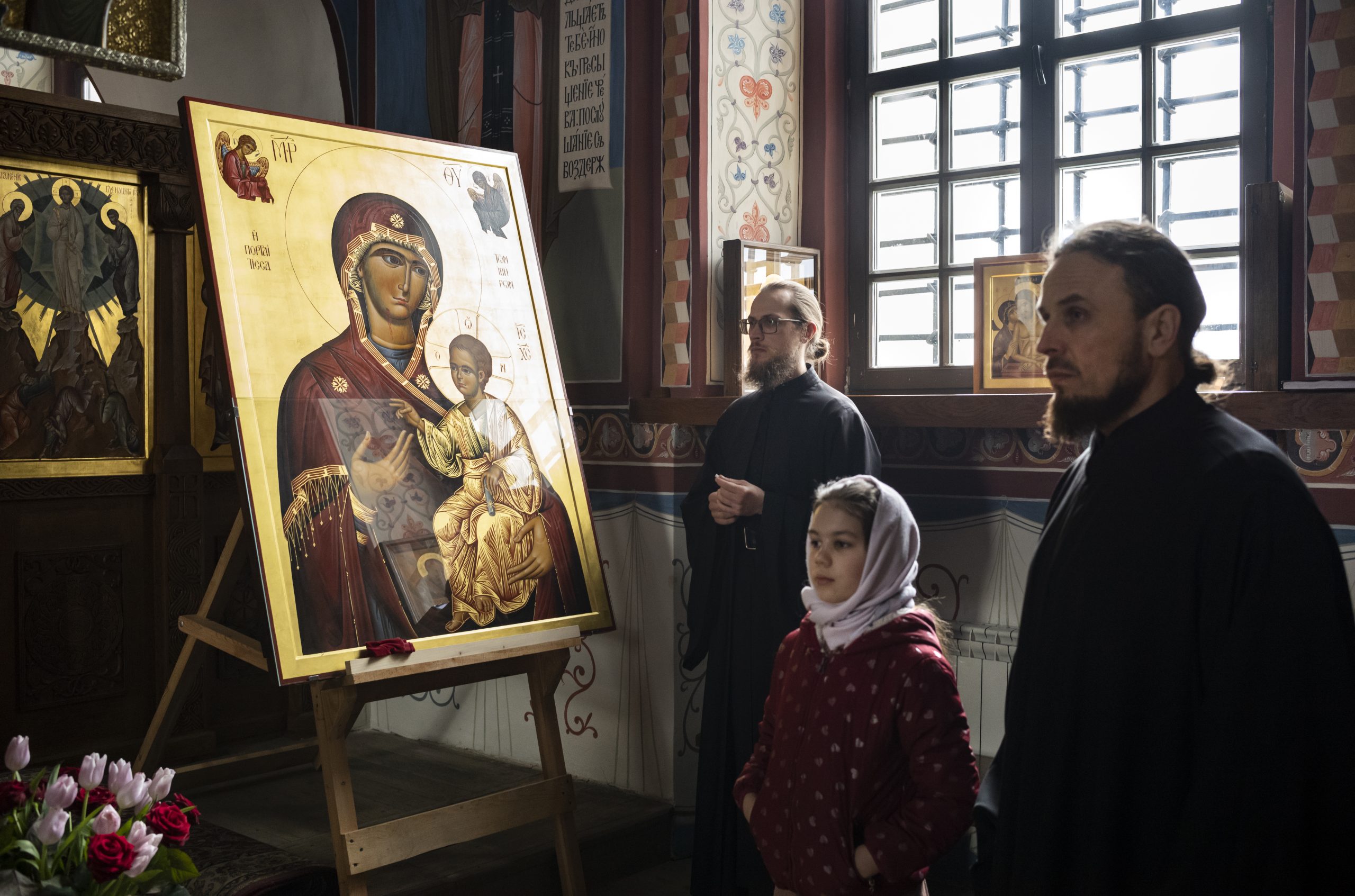 Au monastère de Nescheriv, deux moines prient avec une fillette, entourés par des icônes religieuses orthodoxes.