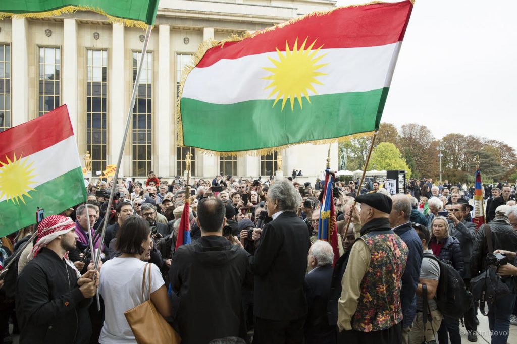 Bernard-Henri Lévy prend la parole lors du rassemblement pour les Kurdes au Trocadéro, face à la foule, sous les drapeaux kurdes.