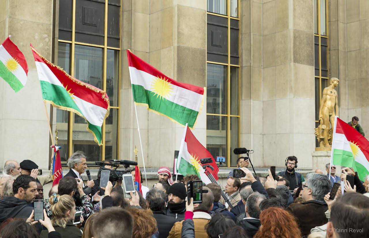 Bernard-Henri Lévy au Trocadéro prend la parole au micro devant la foule sous les drapeaux kurdes, devant les appareils photos et les caméras.