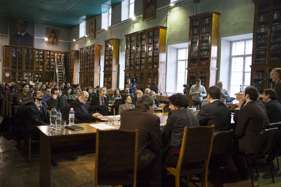 Présentation du Forum européen à l'Université de Kiev le 3 mars 2014. Une table avec des micros est installée devant une bibliothèque. Bernard-Henri Lévy est assis derrière cette table avec d'autres intellectuels. La photos est prise derrière la table, on voit le public dans la bibliothèque de l'Université.
