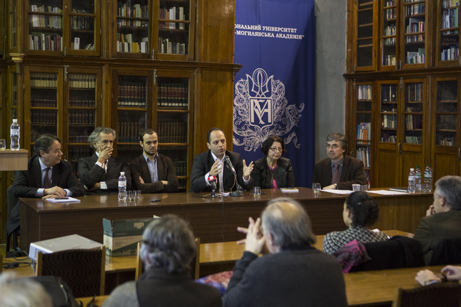 Présentation du Forum européen à l'Université de Kiev le 3 mars 2014. Une table avec des micros est installée devant une bibliothèque. Bernard-Henri Lévy est assis derrière cette table avec d'autres intellectuels.