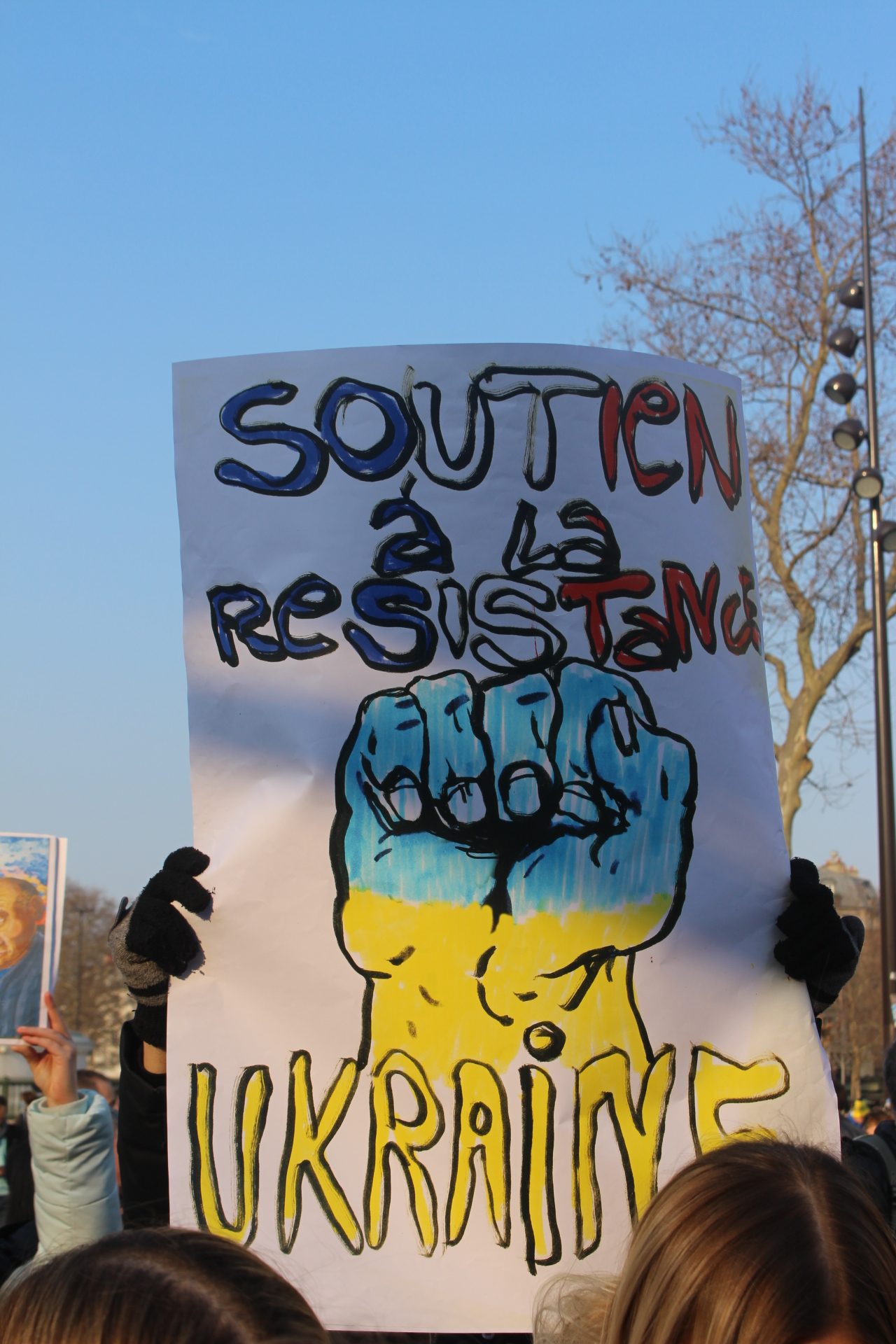 Pancarte représentant un poing levé aux couleurs de l'Ukraine avec l'inscription « Soutien à la Résistance en Ukraine ».