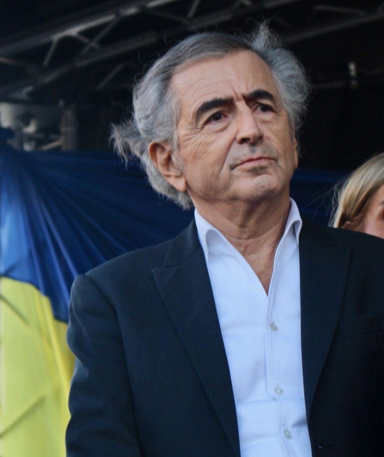 Bernard-Henri Lévy à la tribune de la manifestation pour l'Ukraine, place de la Bastille. Derrière lui on aperçoit un drapeau ukrainien, jaune et bleu.