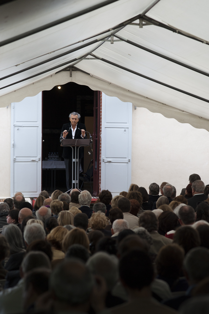Bernard-Henri Lévy à Médan, prononce un discours sur une scène devant la maison de Zola, le public qui l'écoute est installé sous une tente.