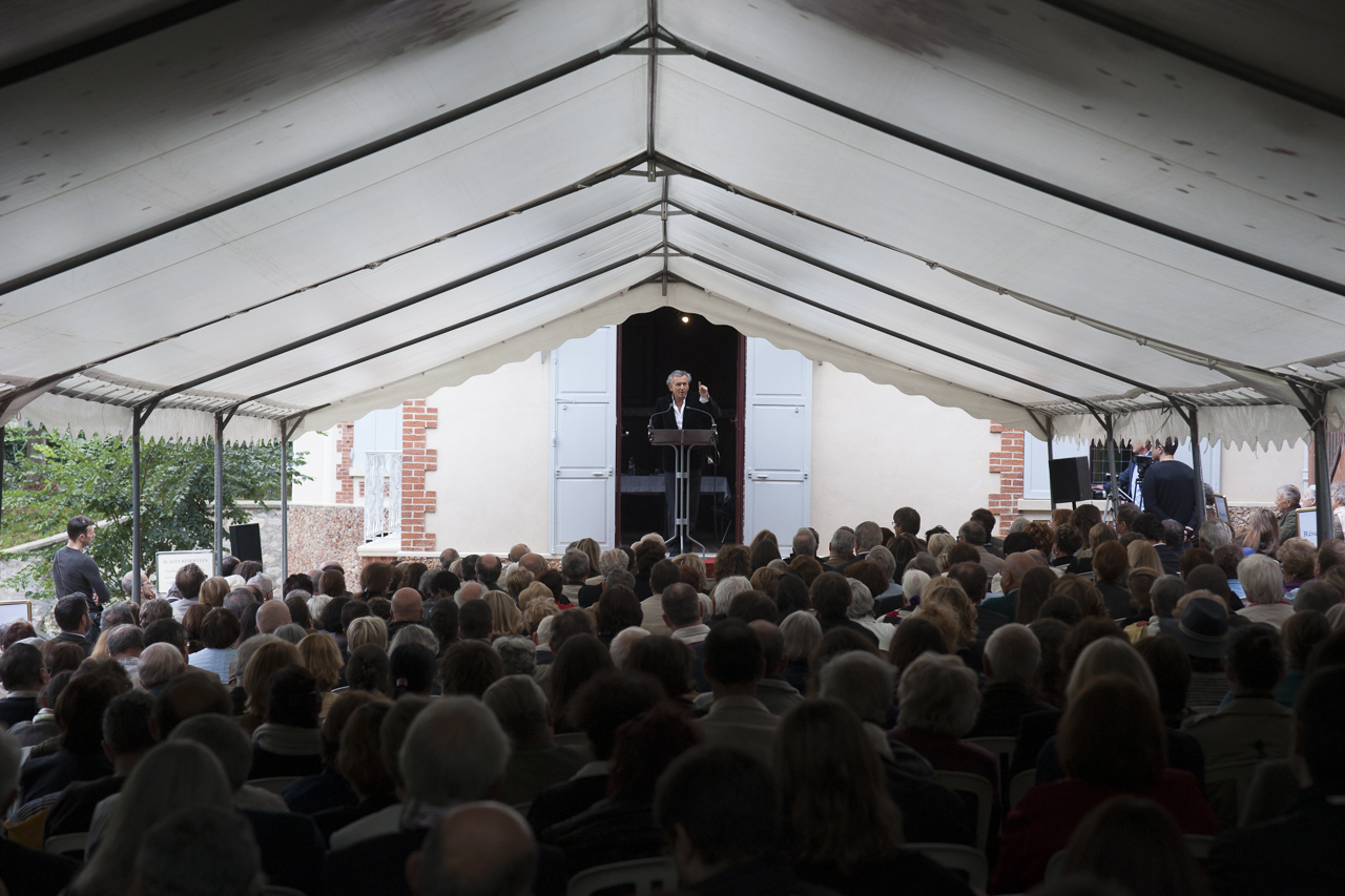 Bernard-Henri Lévy à Médan, prononce un discours sur une scène devant la maison de Zola, le public qui l'écoute est installé sous une tente.