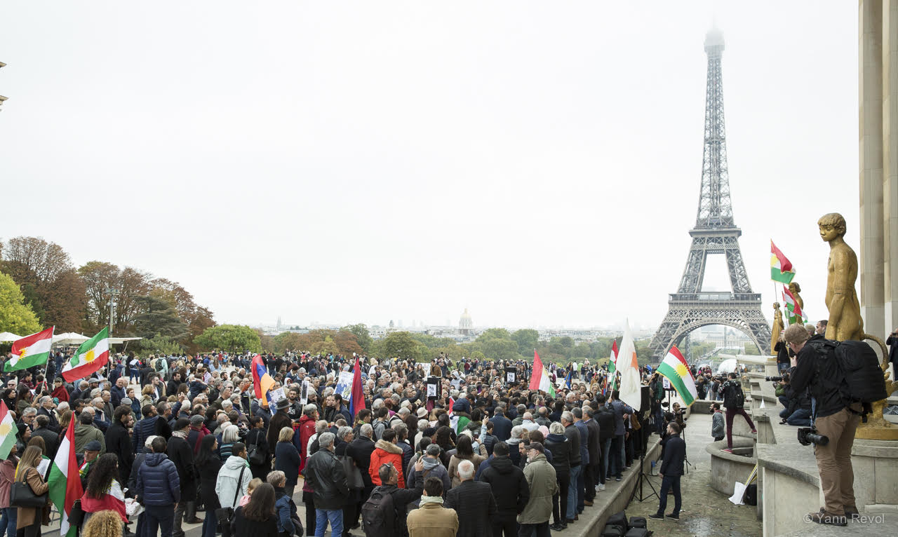 Une foule rassemblée au Trocadéro. Il y a des drapeaux kurdes et la tour Eiffel en arrière plan.