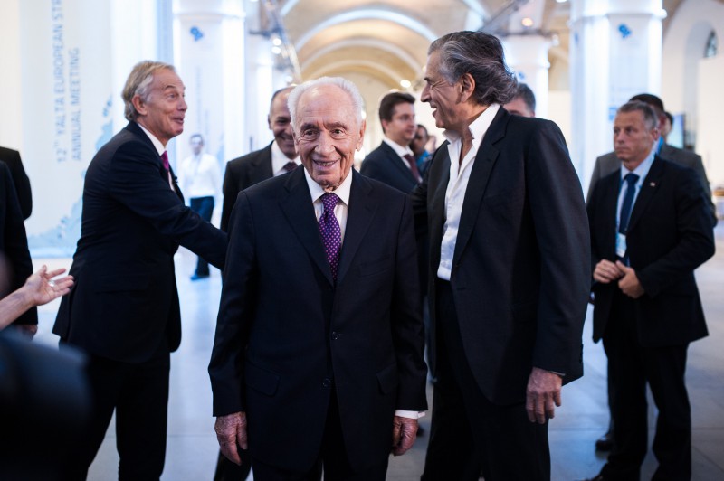 Bernard-Henri Lévy avec Tony Blair et Shimon Pérès au Yalta European Strategy, ils marchent entourés par des hommes en costumes et des journalistes. Tony Blair et BHL se serrent la main.