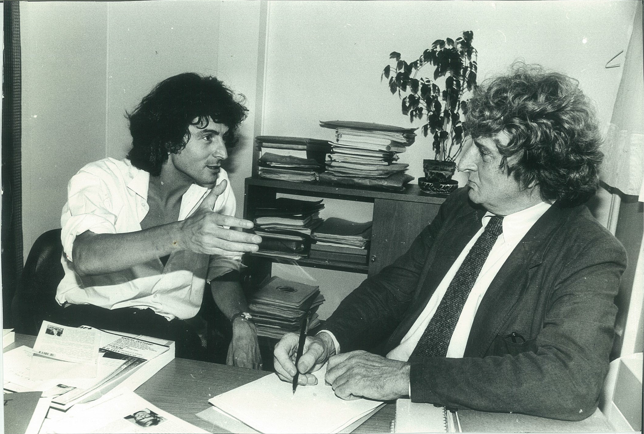 Bernard-Henri Lévy et Paul Guilbert, assis derrière un bureau, ils parlent. Photo en noir et blanc.